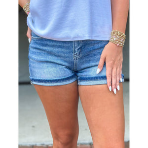 Person wearing blue denim shorts and a light blue top with gold bracelets.