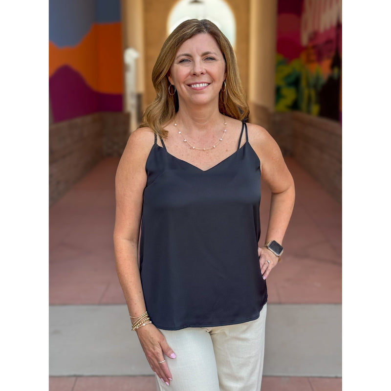 Woman wearing a black top and white pants standing in front of a colorful mural.