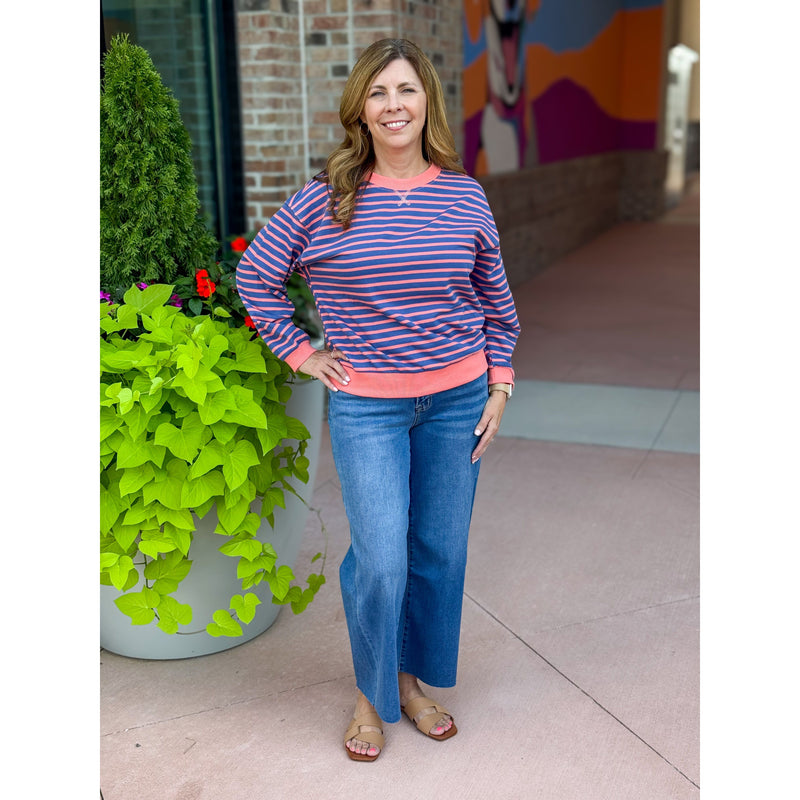 Woman wearing a striped sweater and blue jeans standing in front of a colorful mural.