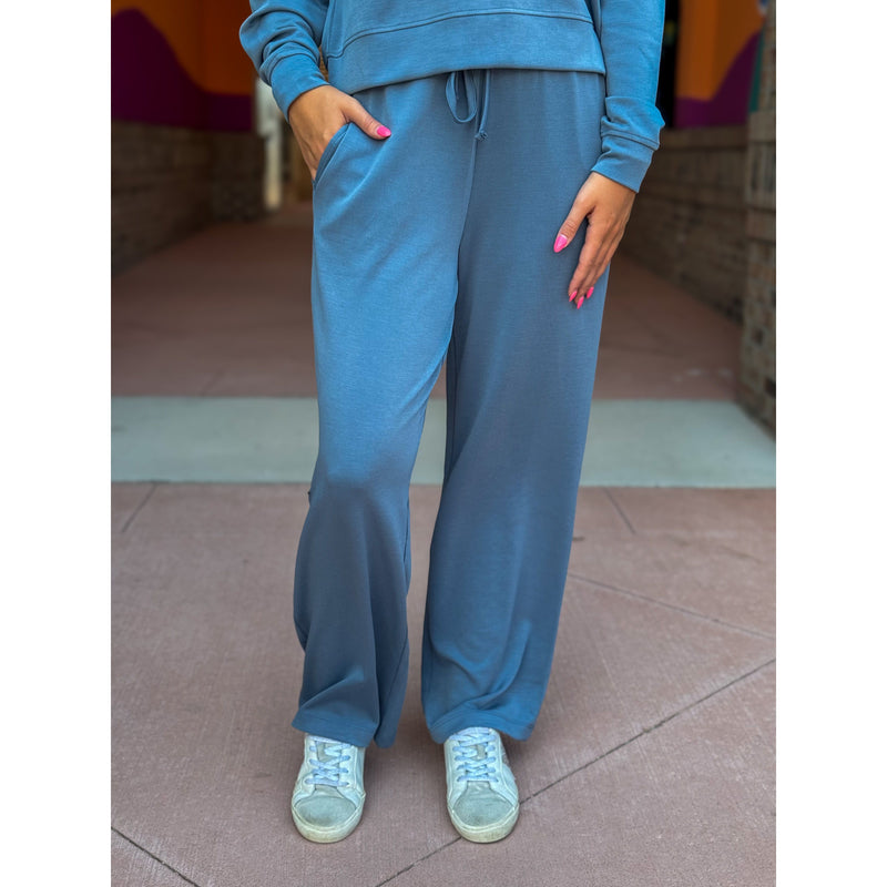 Person wearing a blue tracksuit with wide-leg pants and light blue sneakers on a tiled floor.