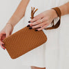Brown woven clutch held by a person with a plain background
