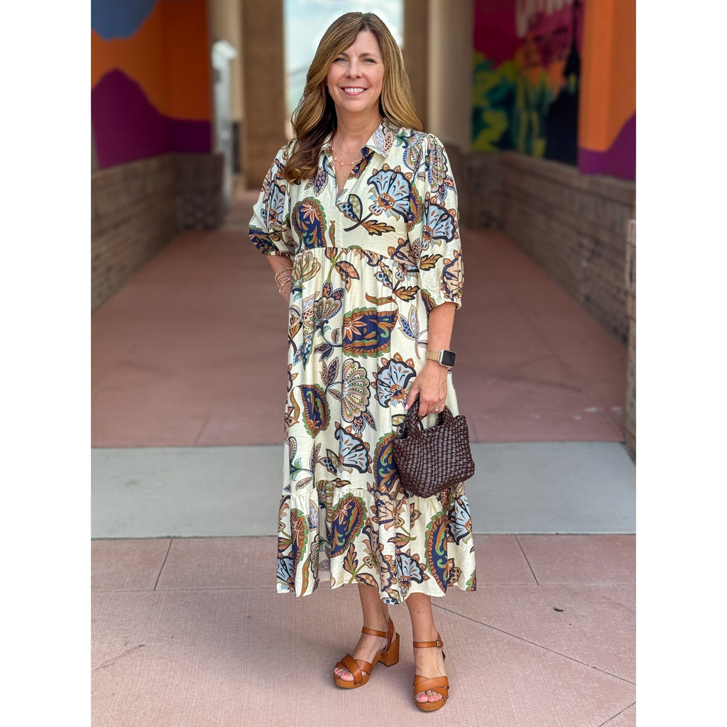 Woman in a patterned dress standing in front of a colorful mural.