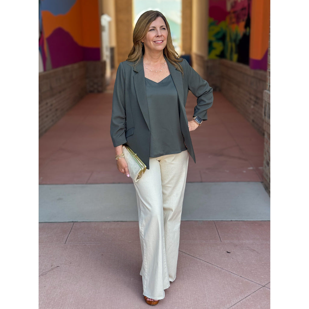 Woman in an olive blazer and ivory pants standing in front of colorful murals.