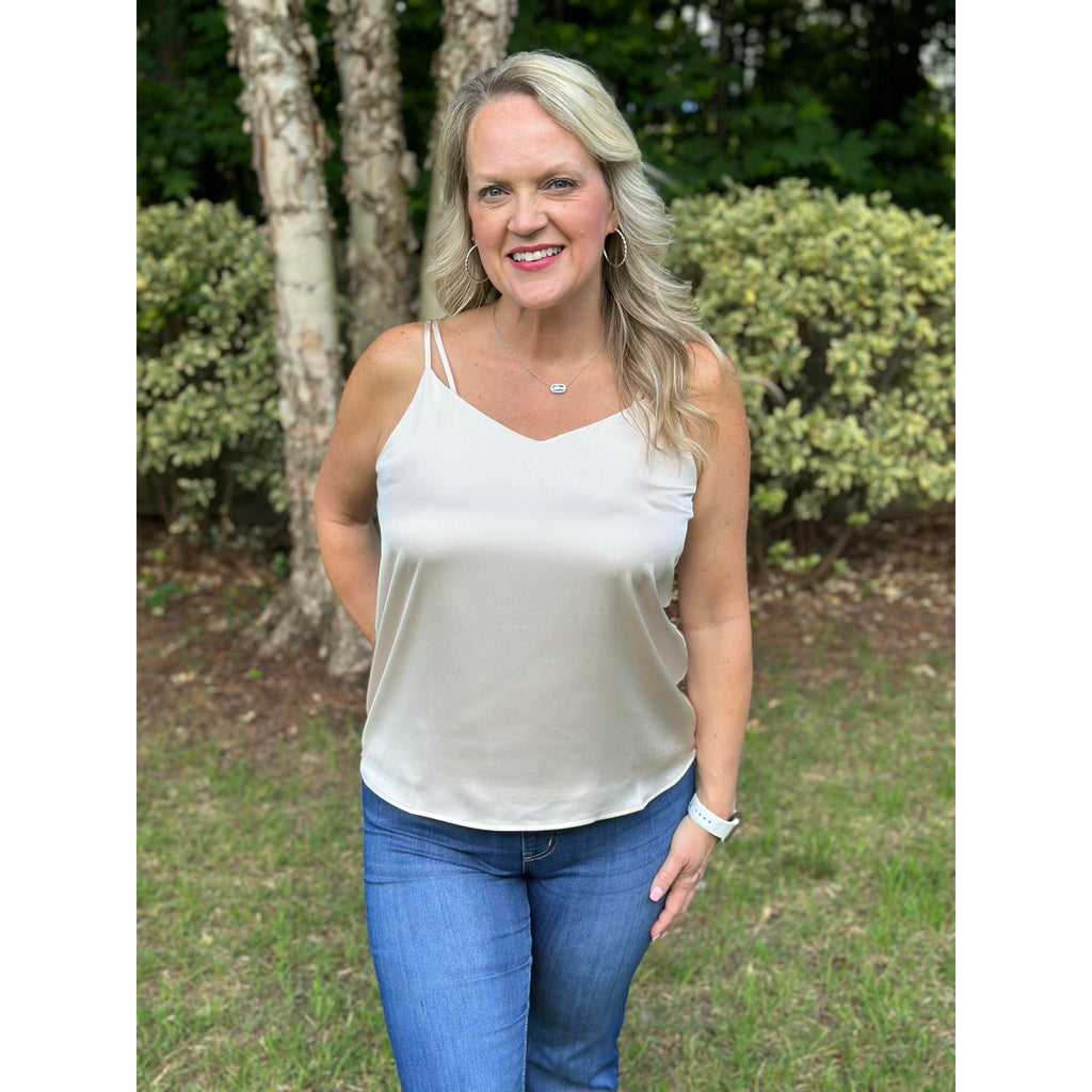 A woman wearing a beige cami top with double straps and a minimal v-neckline, paired with blue jeans.