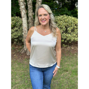 A woman wearing a beige cami top with double straps and a minimal v-neckline, paired with blue jeans.