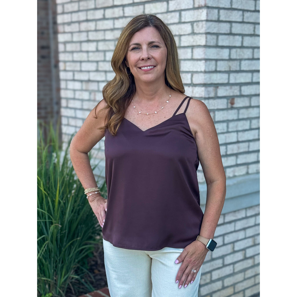 Woman wearing a brown cami and white pants standing in front of a brick wall.
