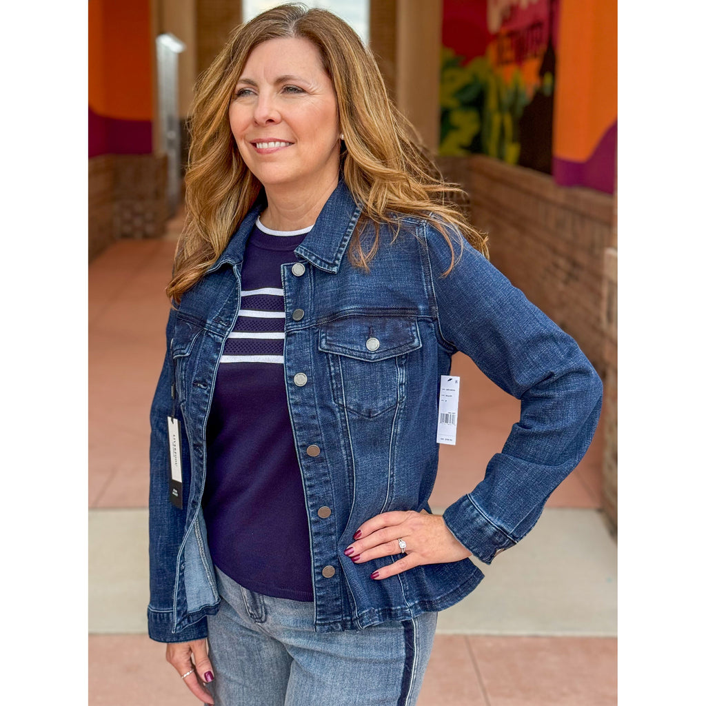 Woman wearing a blue denim jacket with a striped shirt underneath, standing in front of a colorful wall.