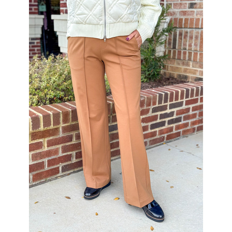 Person wearing tan pants and a white jacket standing in front of a brick wall.