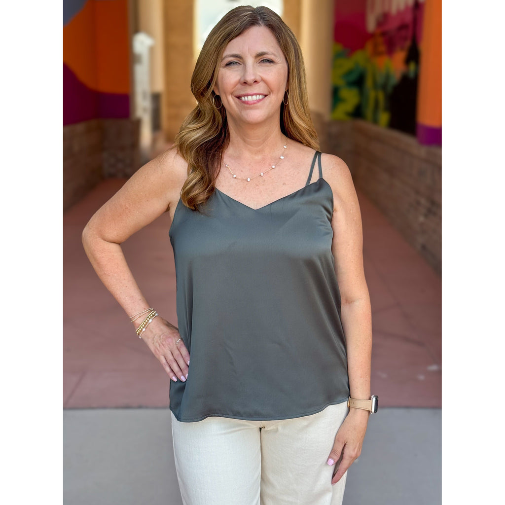 Woman wearing an olive green tank top and white pants standing outdoors with colorful background