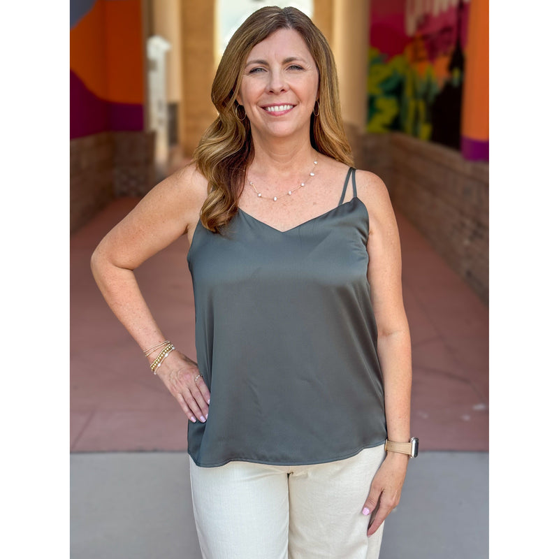 Woman wearing an olive green tank top and white pants standing outdoors with colorful background