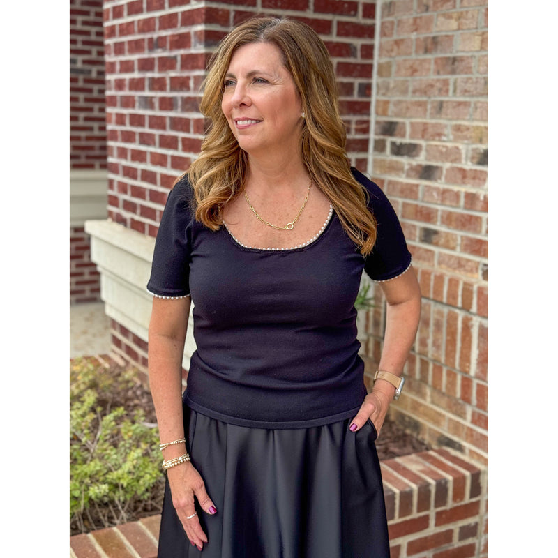 Woman wearing a black top and skirt standing in front of a brick wall.
