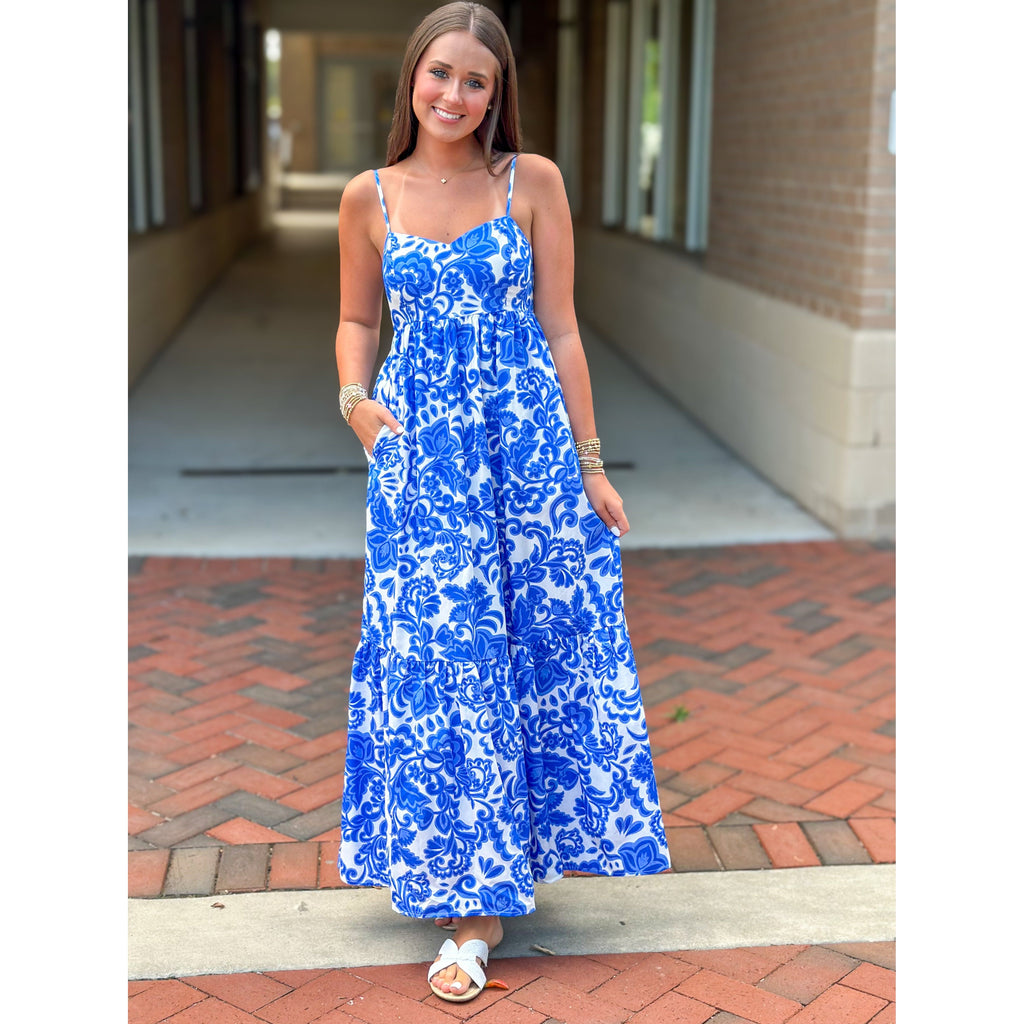 Woman wearing a blue floral dress standing on a brick sidewalk.