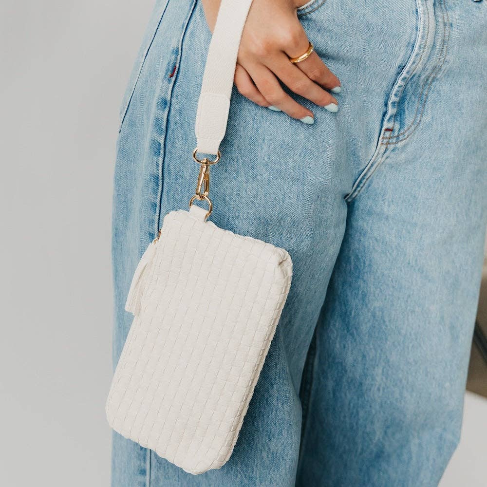 White quilted crossbody bag held by a person wearing light blue jeans.