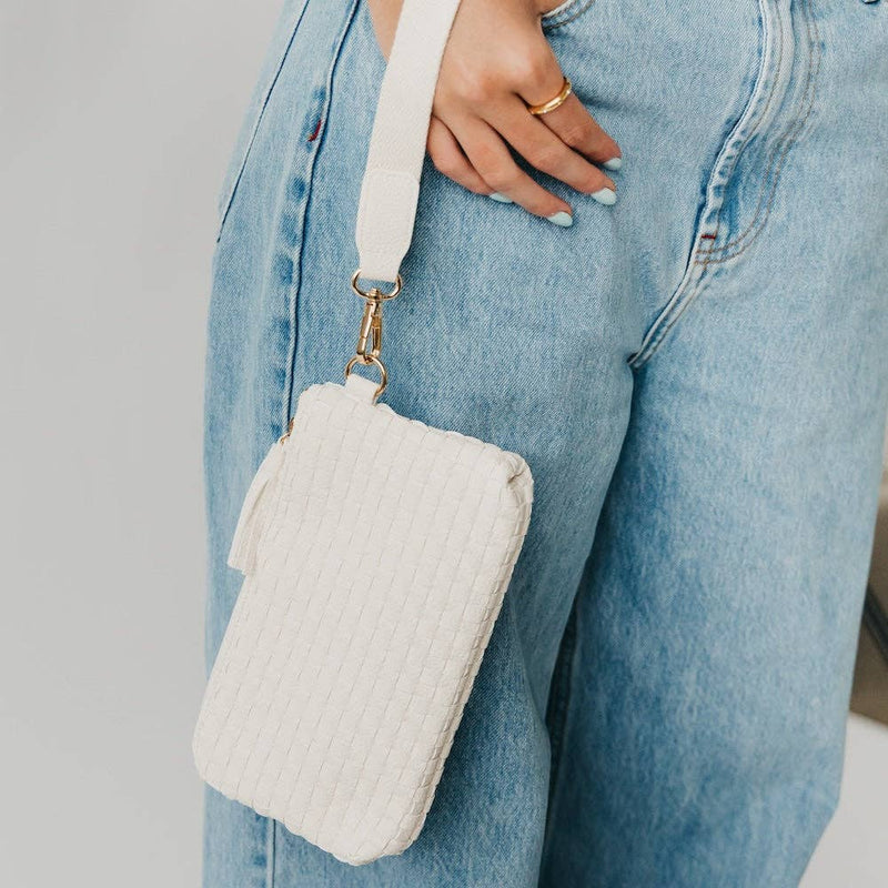 White quilted crossbody bag held by a person wearing light blue jeans.