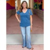 Woman wearing a blue shirt and jeans standing in front of colorful wall art.